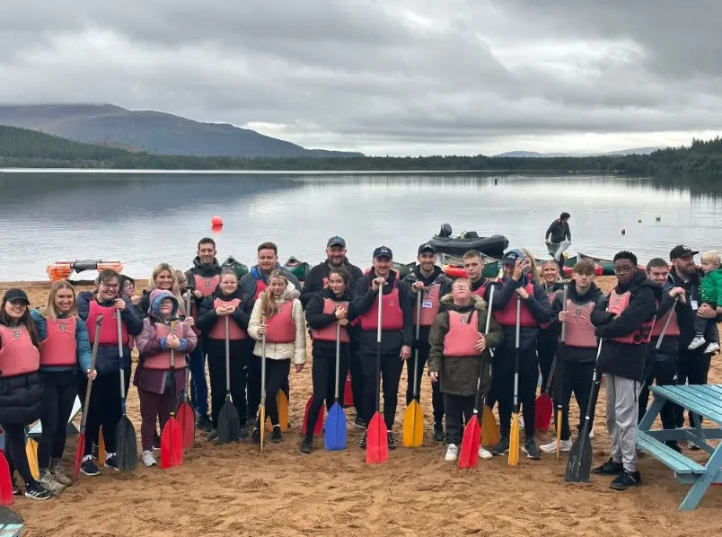 The AWARE Scotland group in buoyancy aids holding paddles on the beach at Loch Morlich